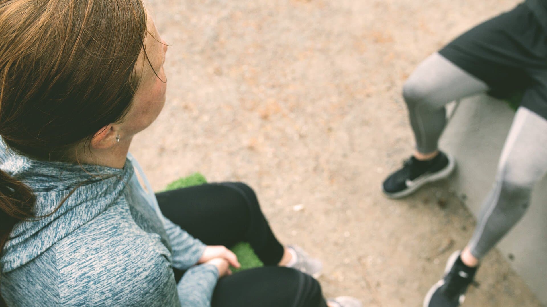 Kvinna i trÀningsklÀder sitter utomhus