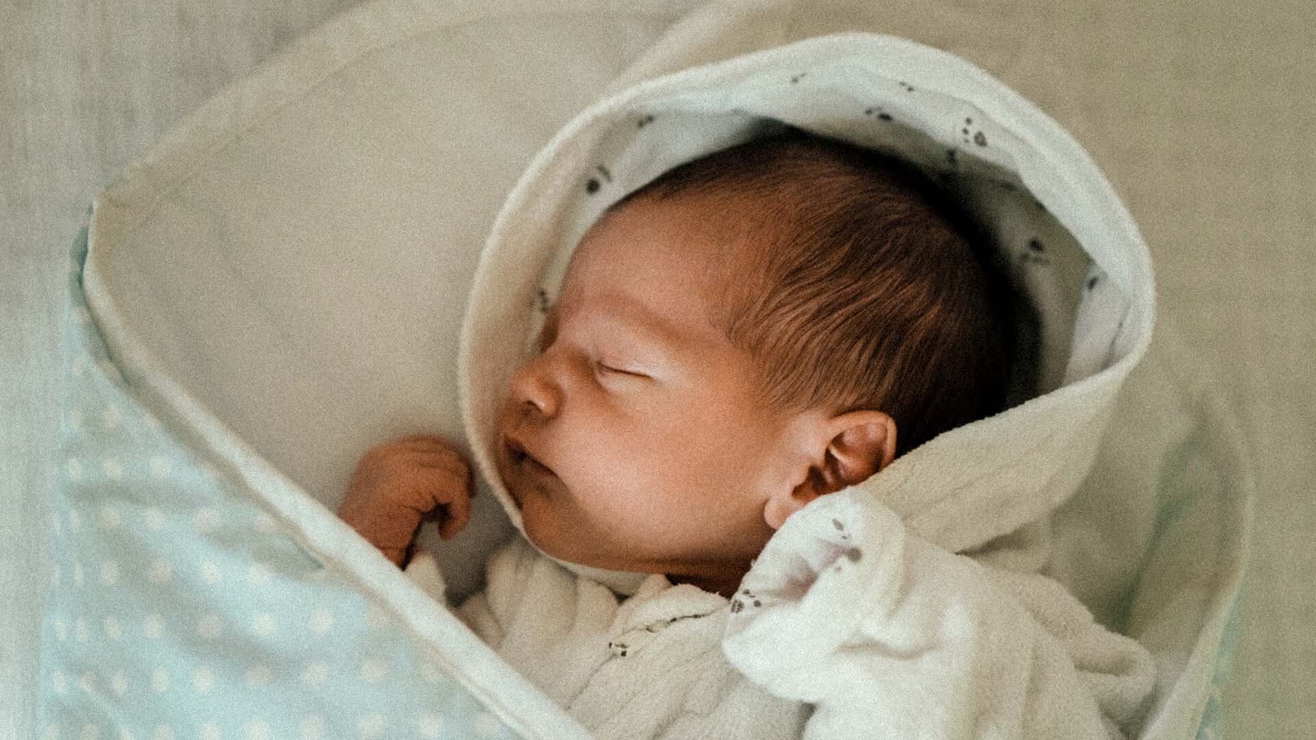 Sovande spädbarn Bebis sover nerbäddad i ljusgrön filt med vita prickar