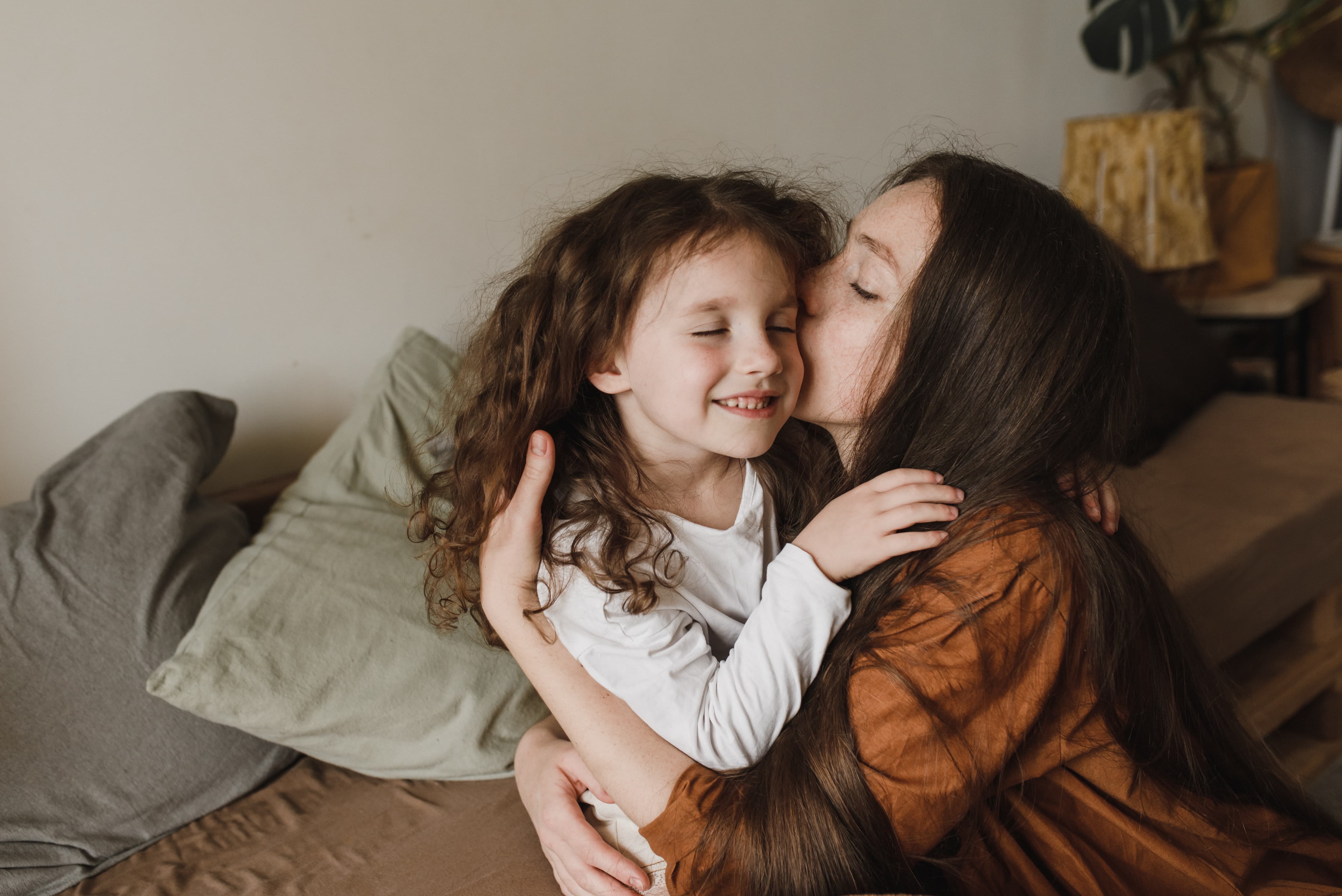 Mor och dotter Leende flicka med lockigt hår blir omfamnad och pussad av sin mamma