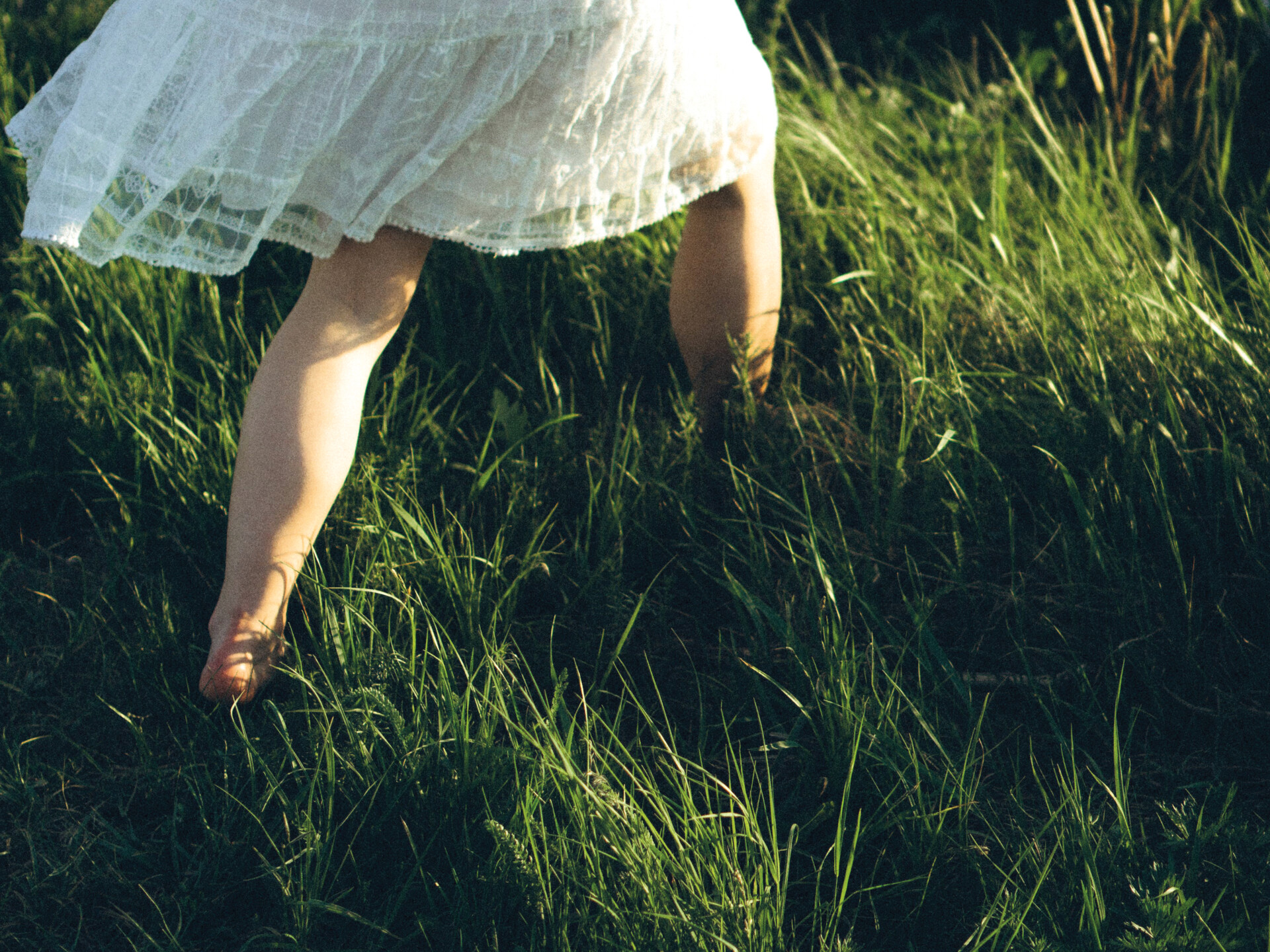 Ett barn går på en äng i högt gräs 
