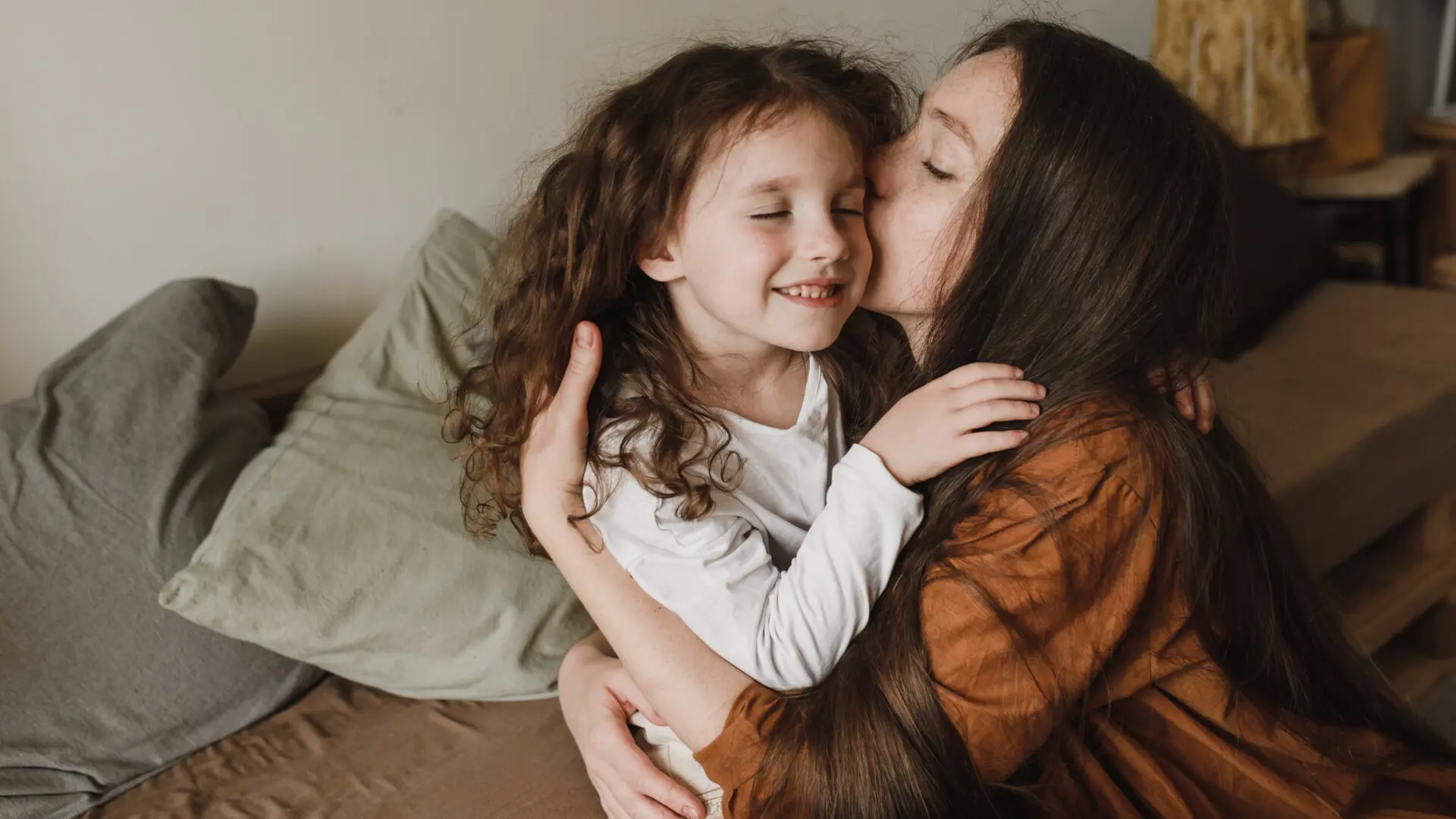 Mor och dotter Leende flicka med lockigt hår blir omfamnad och pussad av sin mamma