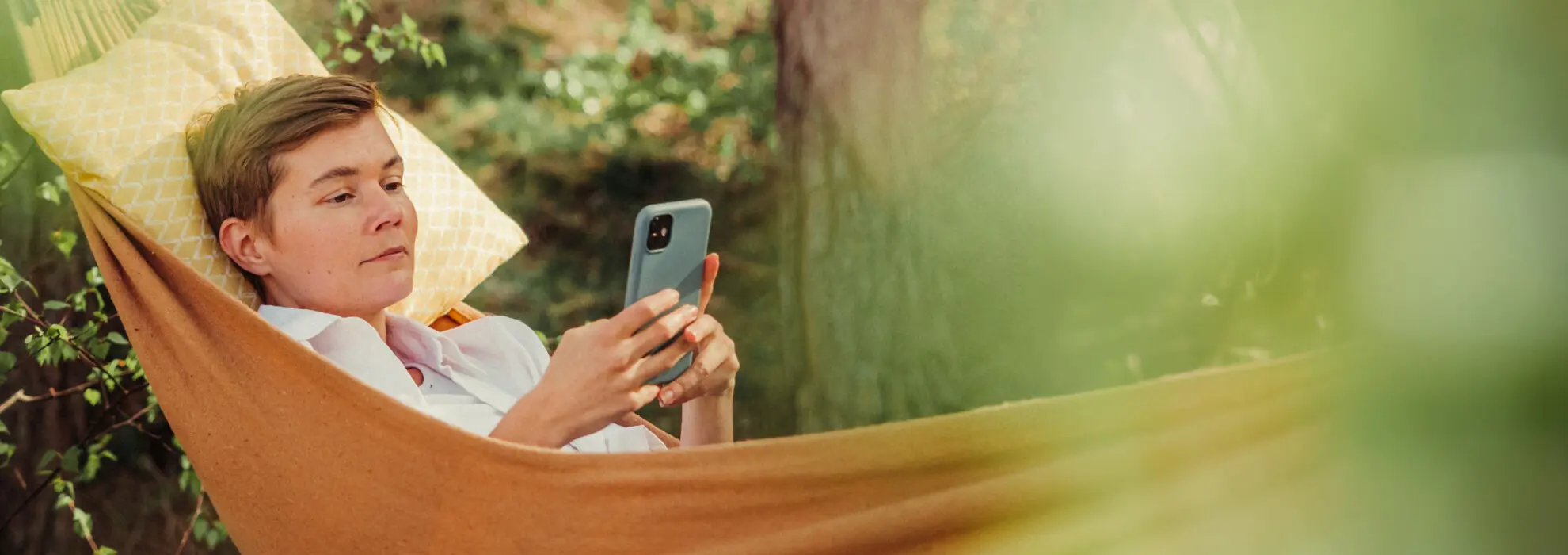 en kvinna som liggeri en hängmatta och scrollar med mobilen