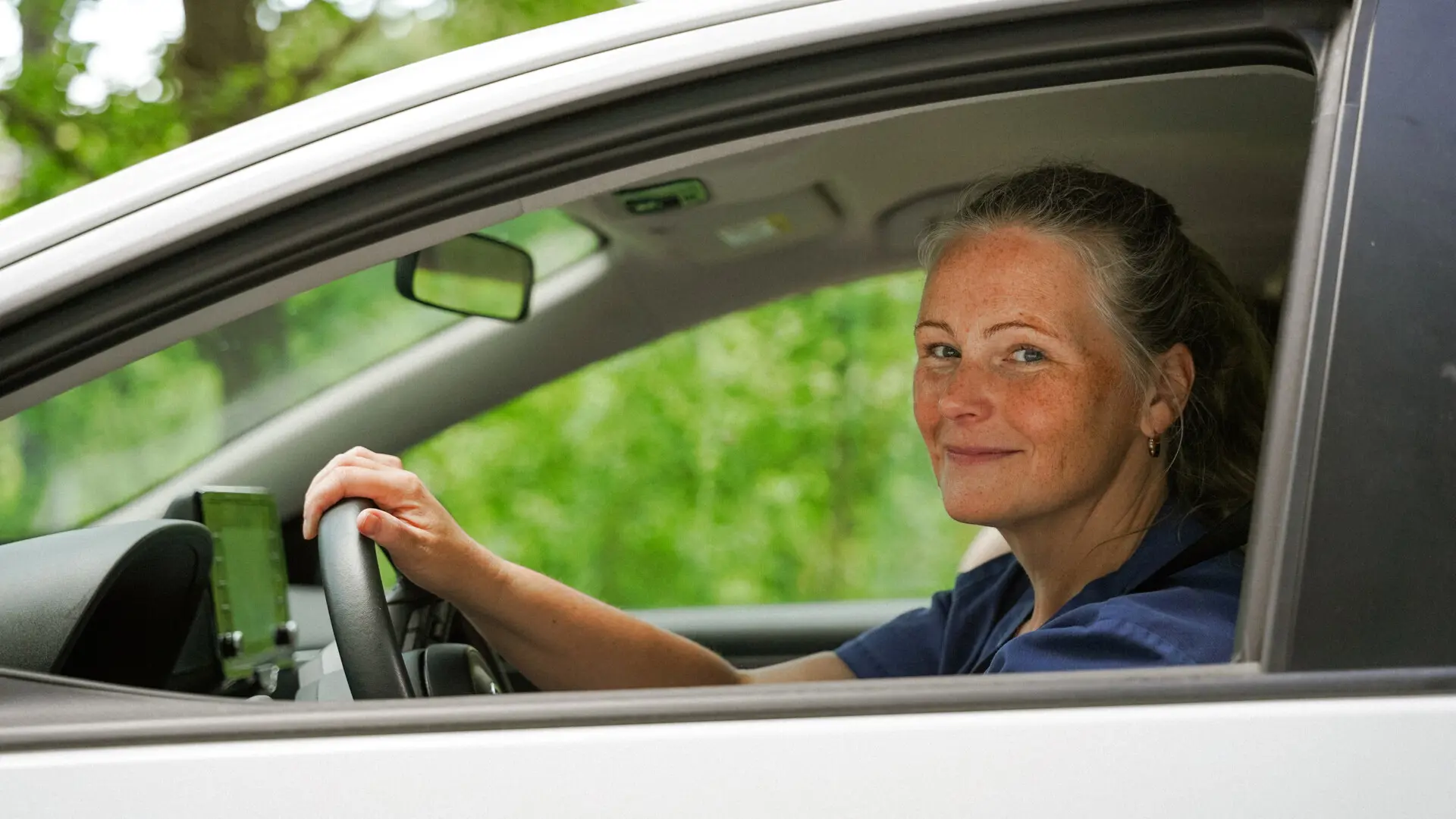 Kvinna i bil som tittar ut genom fönstret och ler